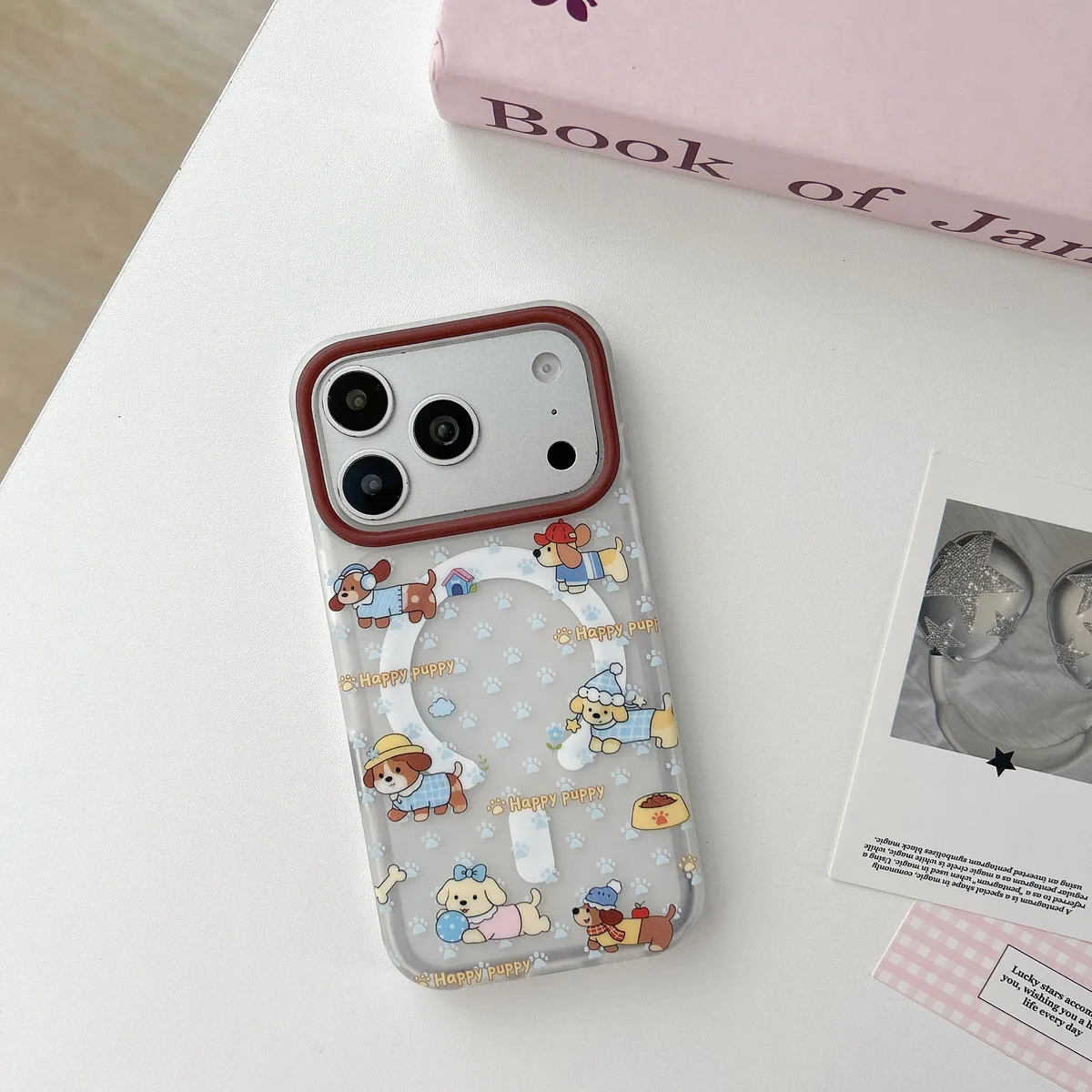 Clear phone case with cartoon puppies, paw prints, and a beaded charm on a light desk