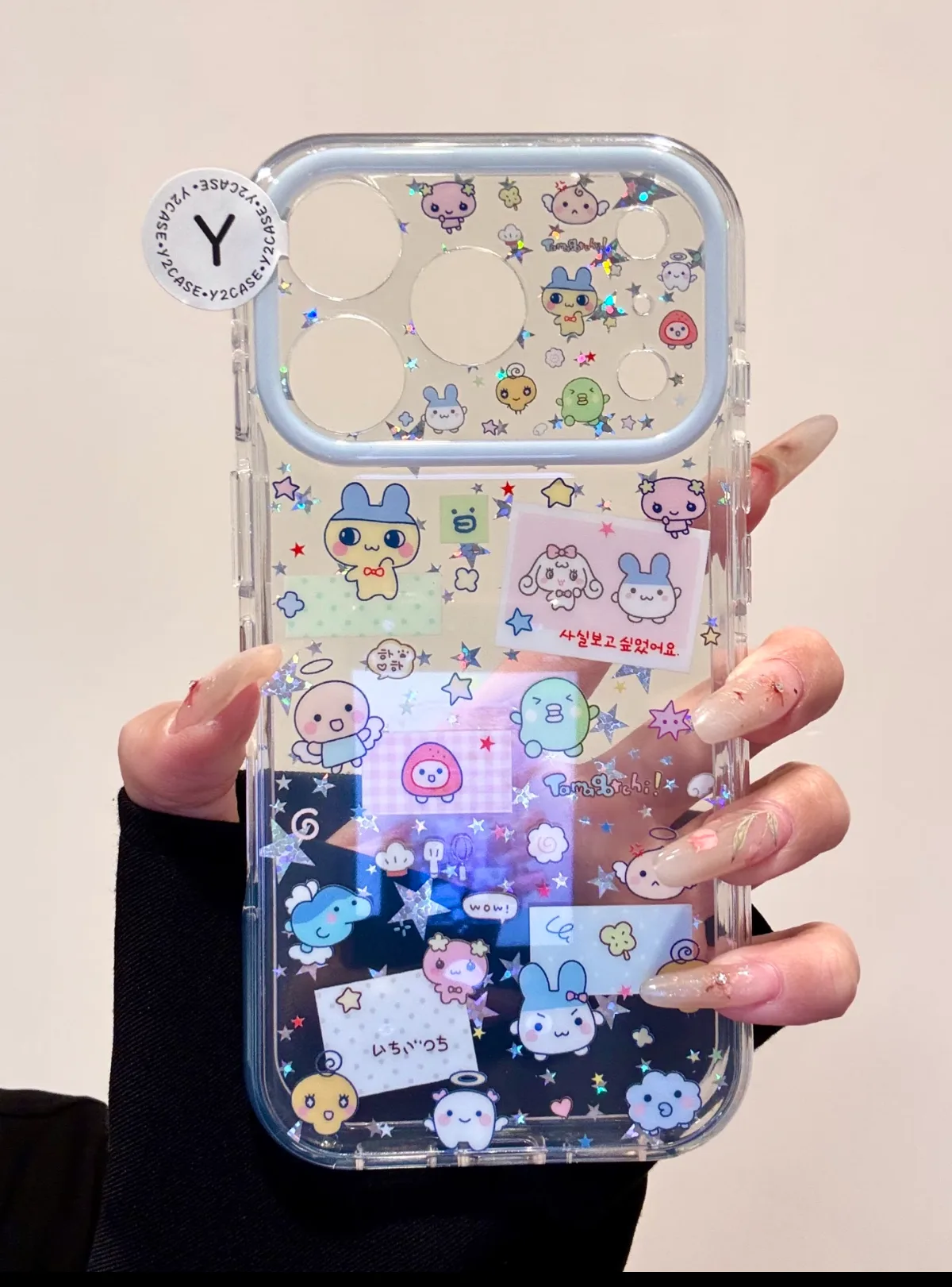 Clear phone case with Tamagotchi characters, glitter, and a beaded strap with star charms.