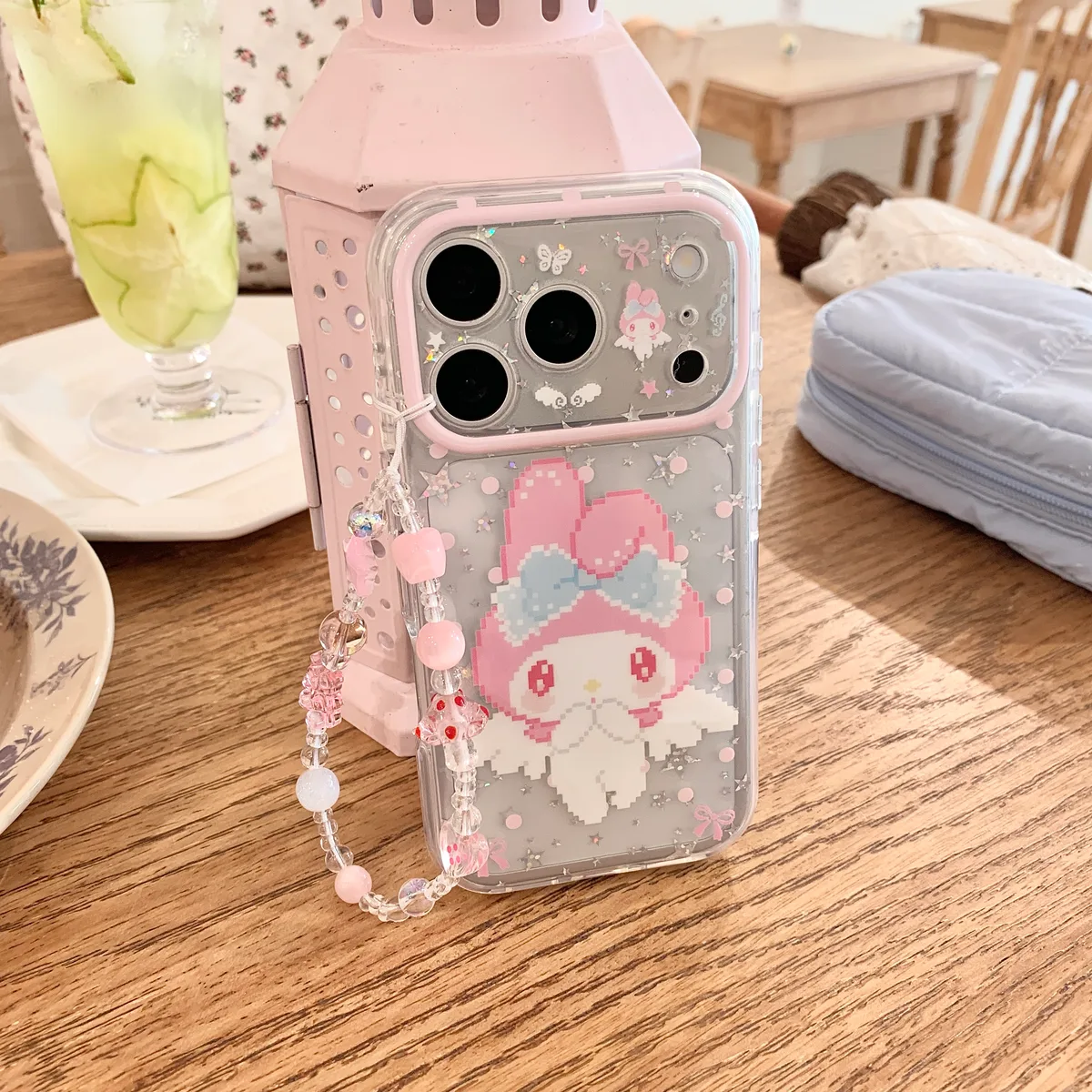 Clear pink My Melody phone case with glitter, bows, and a beaded charm strap on a phone.