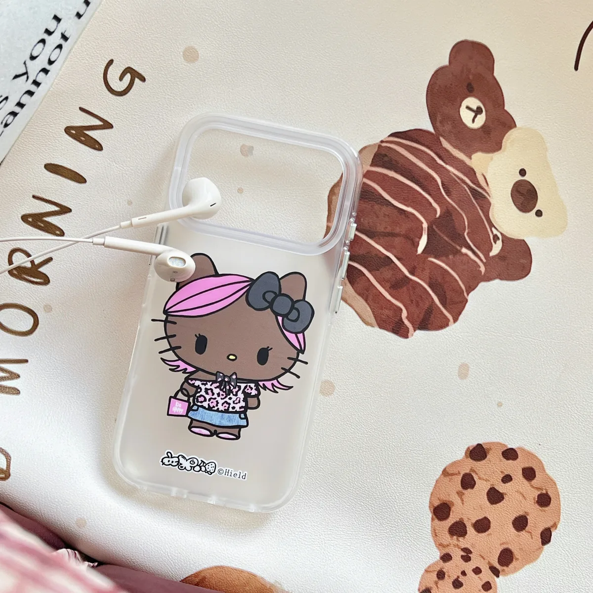 Clear phone case with a black Hello Kitty character wearing a leopard print top and pink hair, placed on a white surface with a pink bag and a drink.