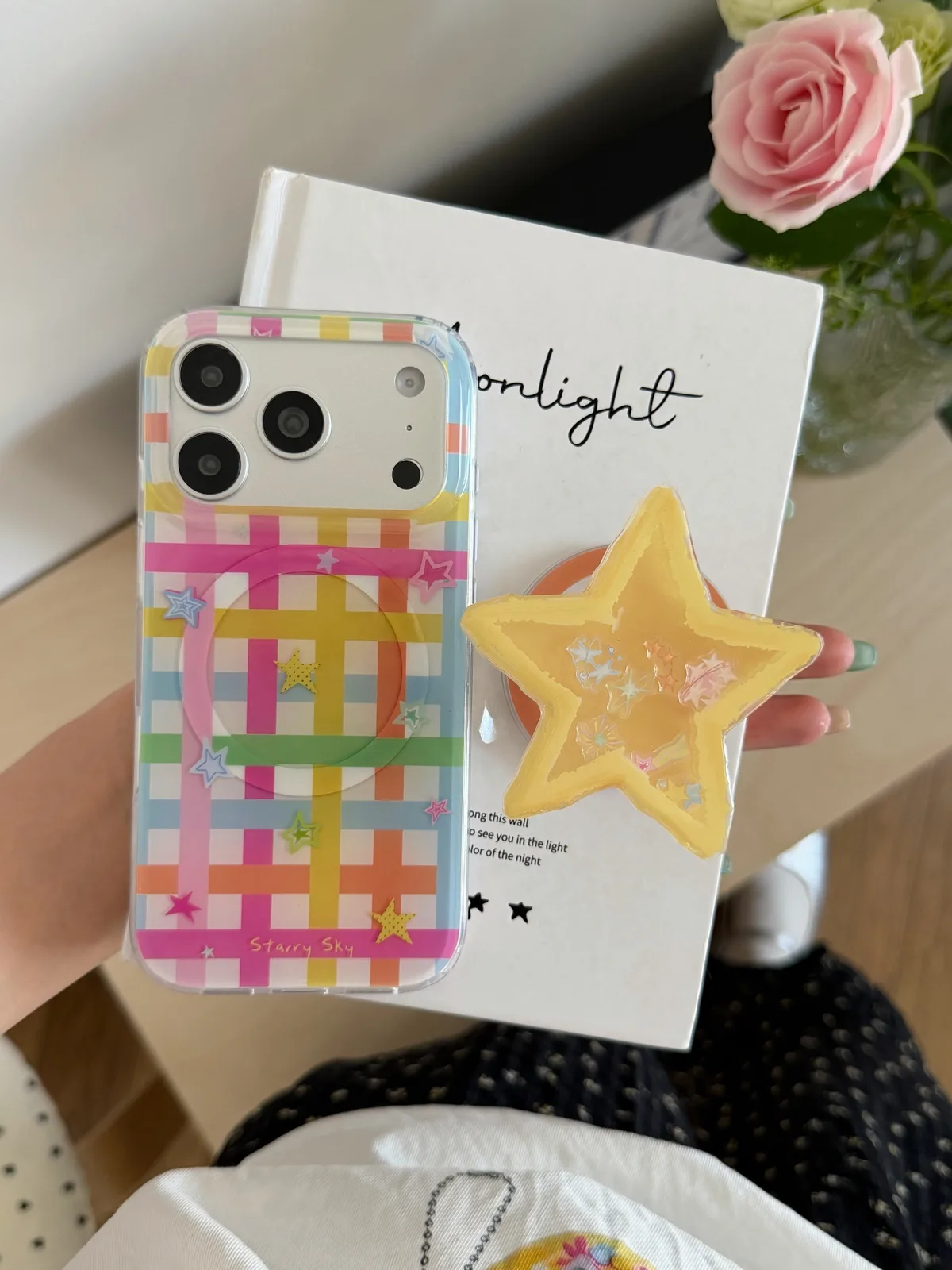 A colorful phone case with a rainbow grid pattern and stars, featuring a MagSafe ring and a yellow star-shaped stand attached to the back.