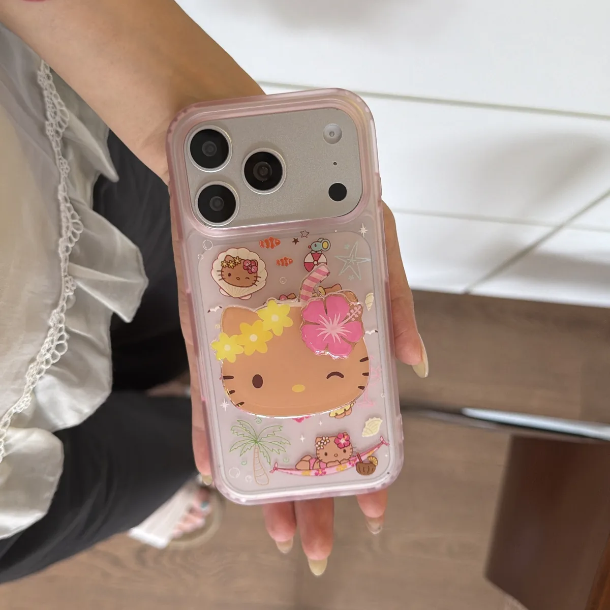 A clear pink iPhone case with Hello Kitty in a tropical summer design, featuring flowers, palm trees, and a hammock,