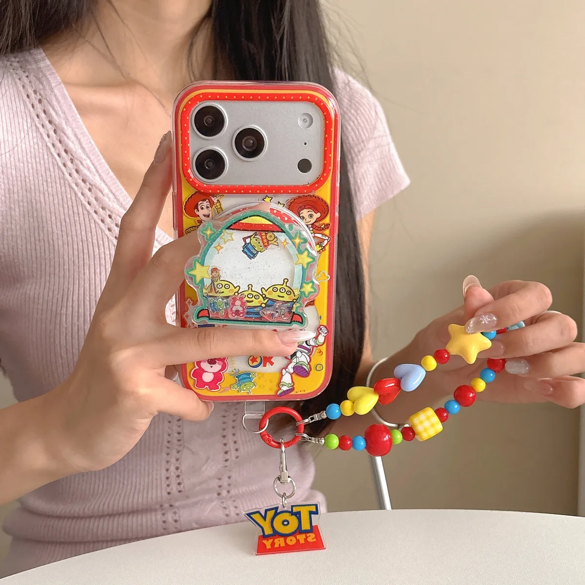 A person holding a clear iPhone case with a Toy Story water slide game design and a colorful beaded strap.