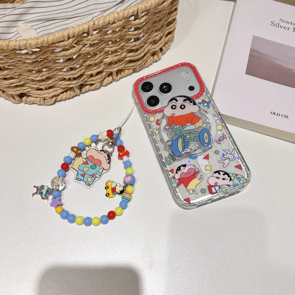 Clear iPhone case with Crayon Shin-chan design, colorful beaded strap, and pop socket, held in hand and displayed on a