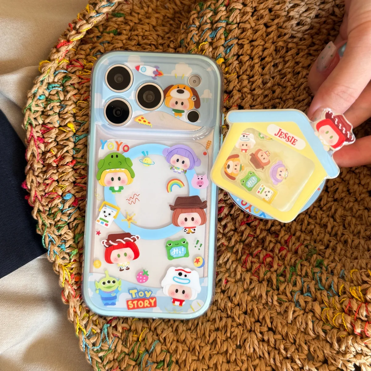 A light blue and clear phone case with Toy Story characters and a house-shaped charm, shown with a beaded strap.