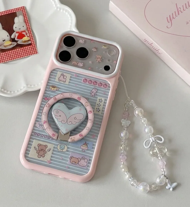Pastel pink phone case with winged heart art, a circular grip stand, and a beaded strap